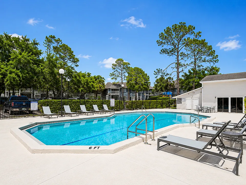 Inviting outdoor pool area with modern lounge chairs, surrounded by lush greenery and clear blue skies.