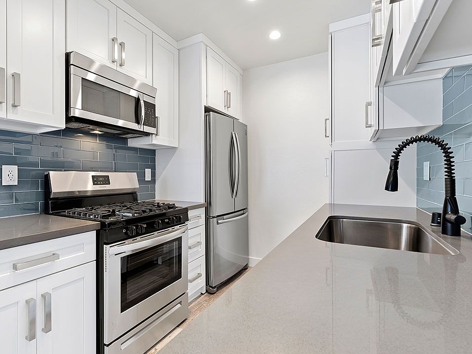 Blue tiled kitchen with quartz stone counters and stainless steel microwave, oven, fridge, and fixtures.