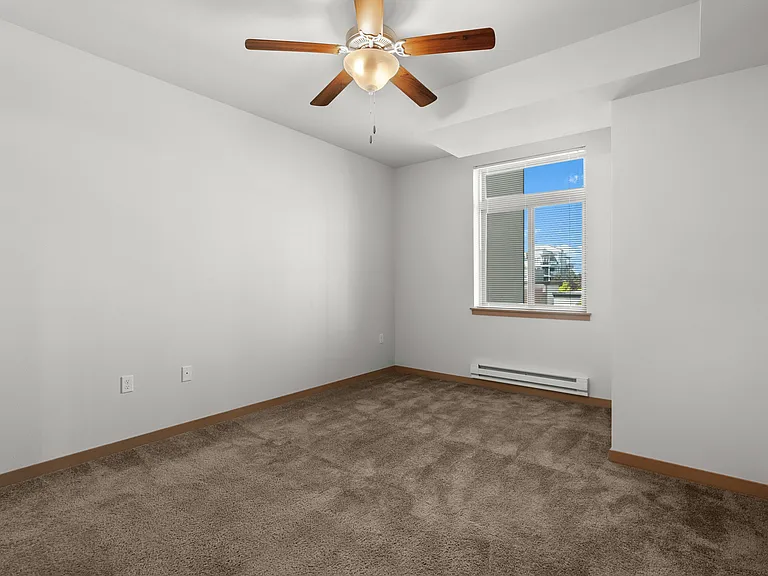 Bright and inviting empty bedroom with plush carpeting and a ceiling fan, offering a serene atmosphere with natural light streaming through the window. Bright and inviting empty bedroom with plush carpeting and a ceiling fan, offering a serene atmosphere