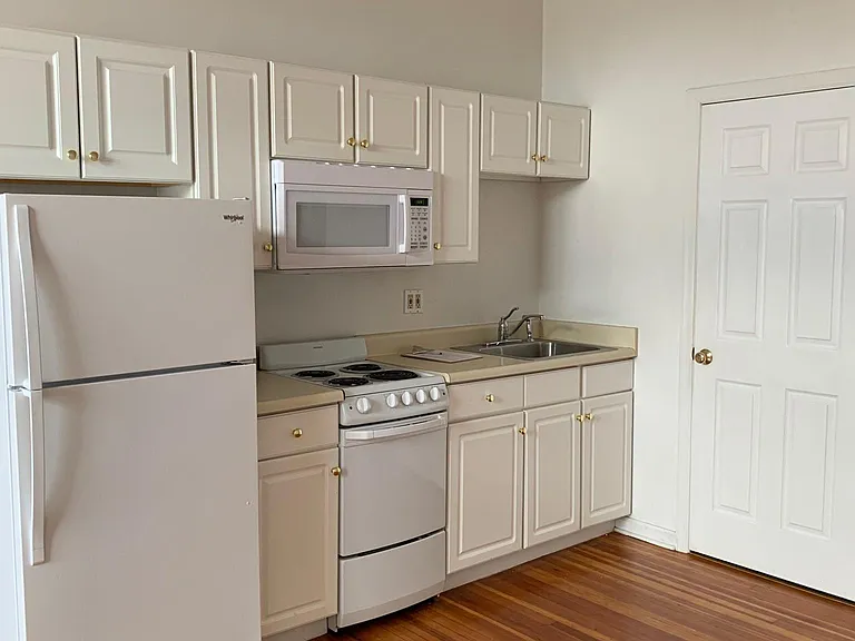 Kitchen space, white appliances and white cabinets, wood floor.