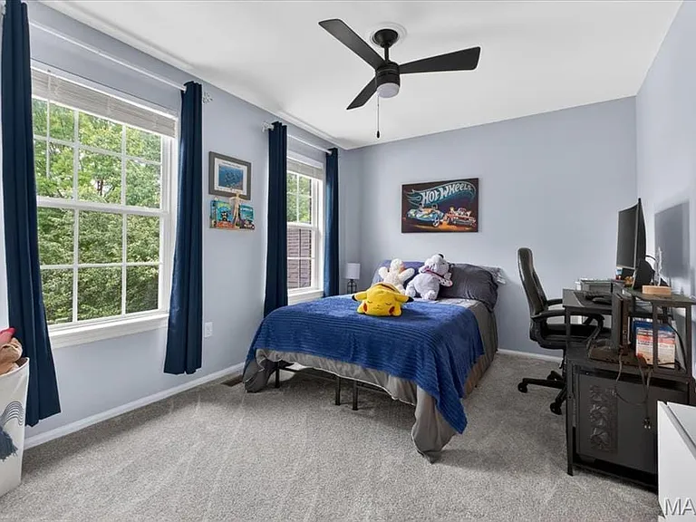 Room featuring two large windows, light blue wall paint, gray carpet flooring, a black ceiling fan, and built-in shelving