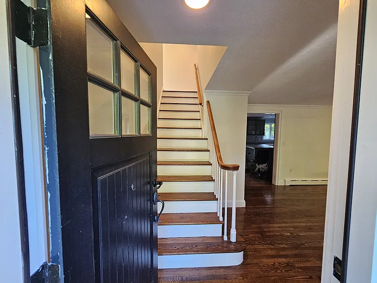 The front door opens into the main level, with the staircase to the upper floor directly ahead and the living room visible beyond.