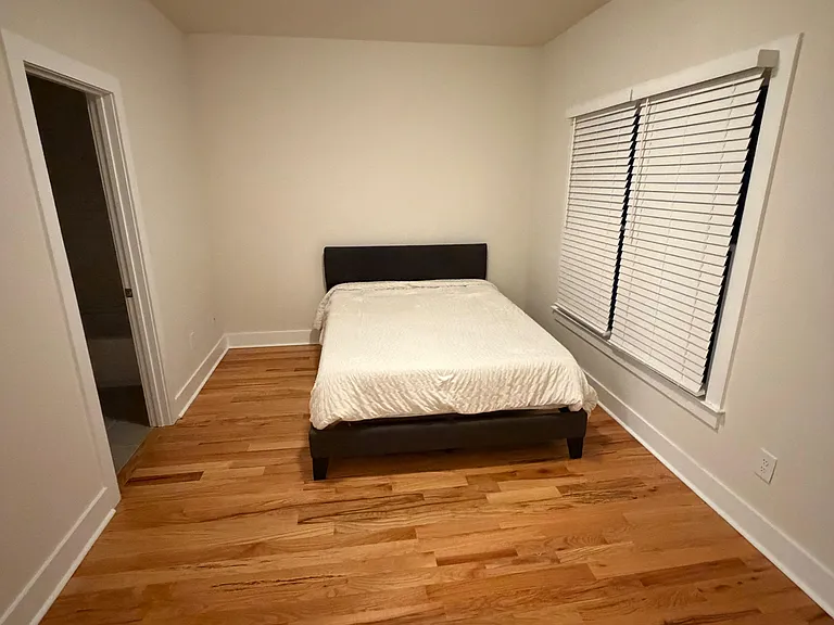 Private bedroom with hardwood floors, overhead lighting, and a large window with blinds for adjustable privacy.