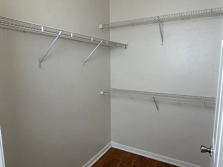 Spacious walk-in closet with sleek white wire shelving and wood-style flooring, ideal for organized storage solutions. Spacious walk-in closet with sleek white wire shelving and wood-style flooring, ideal for organized storage solutions.