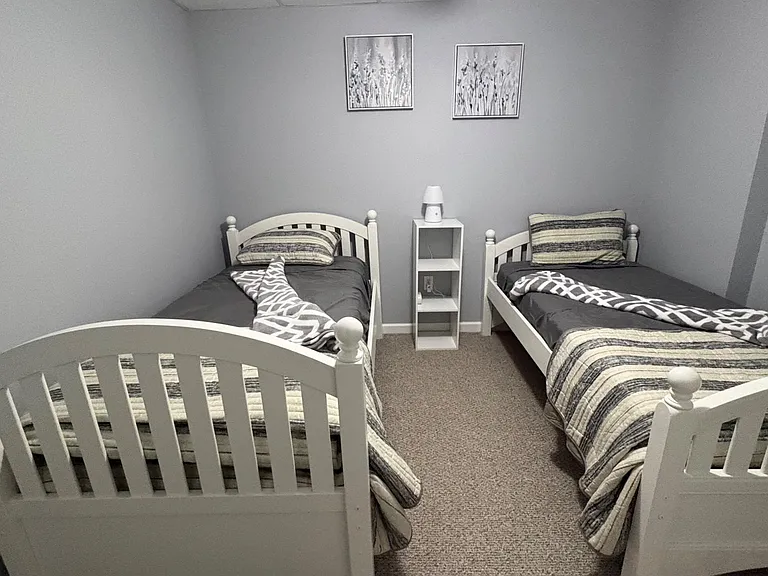 Shared bedroom setup with two twin beds, carpeting, and a small shelving unit for bedside storage.