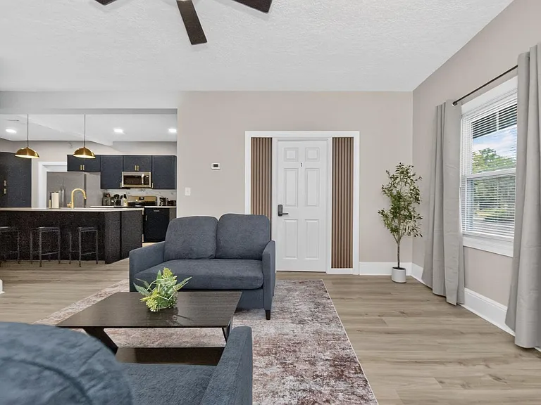 Open-concept living area with a comfortable seating zone, large window, and direct flow into the kitchen with bar seating.