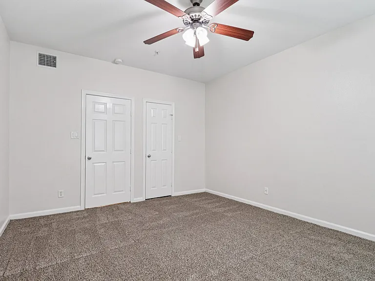 Spacious bedroom with plush carpet, dual white doors, and elegant ceiling fan lighting. Spacious bedroom with plush carpet, dual white doors, and elegant ceiling fan lighting.