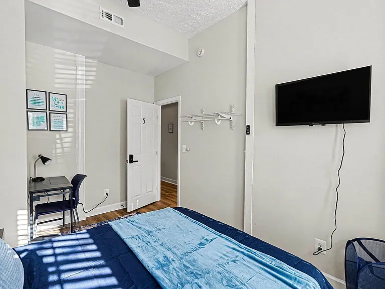 Furnished private bedroom with a work desk, wall-mounted TV, and convenient shelving for everyday storage.