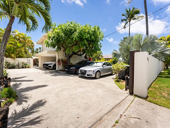 Gated entrance to the property featuring a spacious driveway, covered carport parking, and lush tropical landscaping for added privacy and curb appeal.