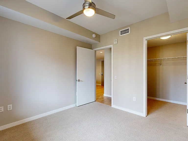 Spacious apartment bedroom with large closet and plush carpet flooring.