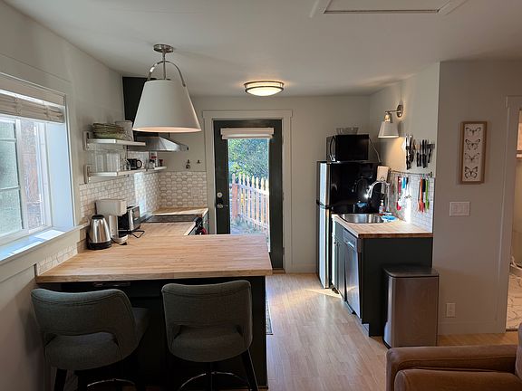 Kitchen with butcher block counters, open shelving, range, refrigerator, microwave, dishwasher and bar seating for two