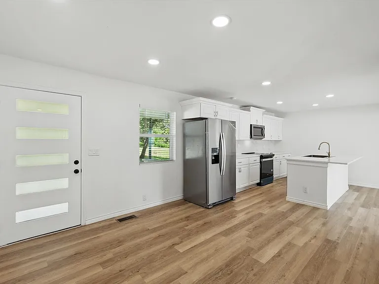 Kitchen with appliances with stainless steel finishes, a sink, light wood-style floors, white cabinets, and light countertops