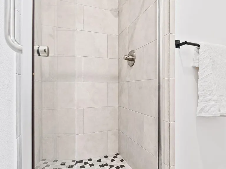 Walk-in glass-enclosed shower with large-format tile surround, mosaic shower pan, and modern fixtures for easy upkeep.