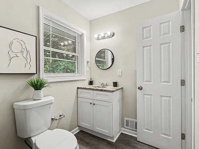 Updated bathroom with a granite-top vanity, modern lighting, and a window with blinds for natural light and ventilation.