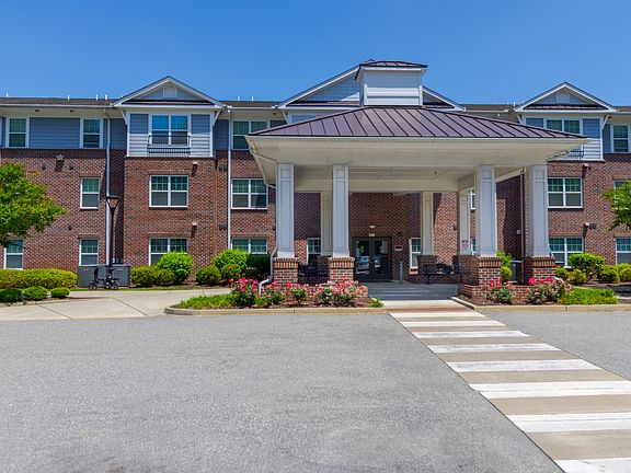 Front entrance of Snowden Senior Apartments featuring a large covered portico, landscaped walkway, and accessible crosswalk for residents and guests.