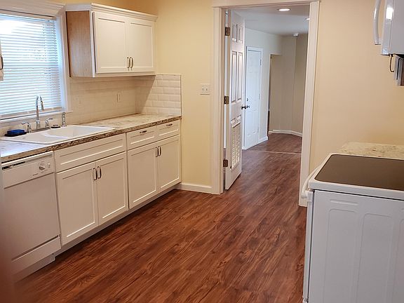Open kitchen with new stove, microwave, dishwasher, counter, sink and cabinets.