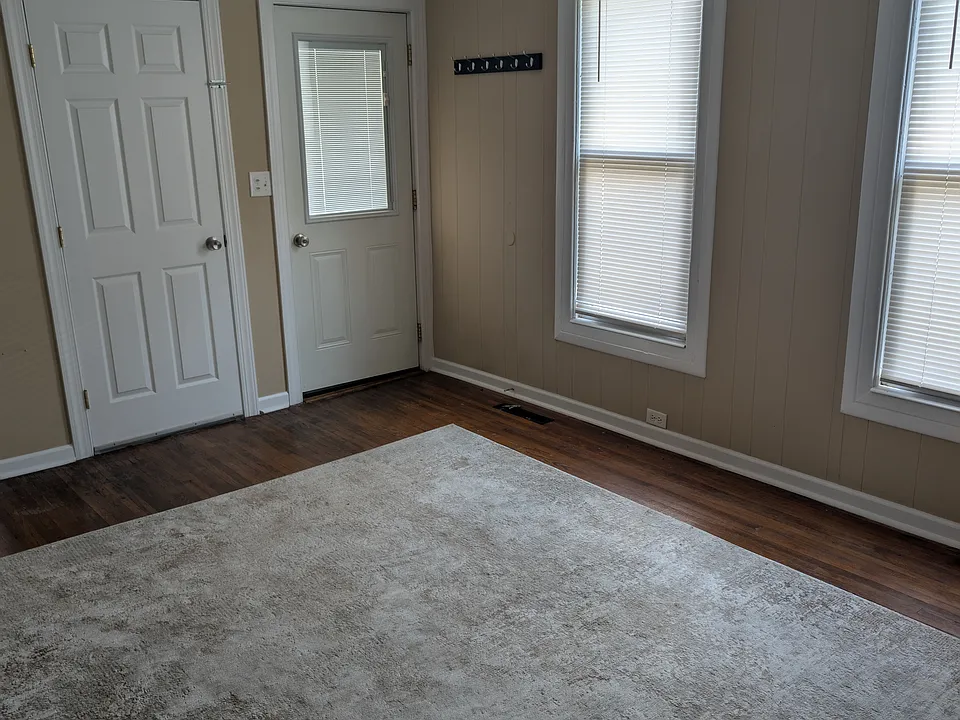 Dining room (showing entrance door and door to basement. This room has a tray ceiling with a ceiling fan, two windows with mini blinds, hardwood floor and area rug. Walls painted in neutral color. Room size: 11 x 15.