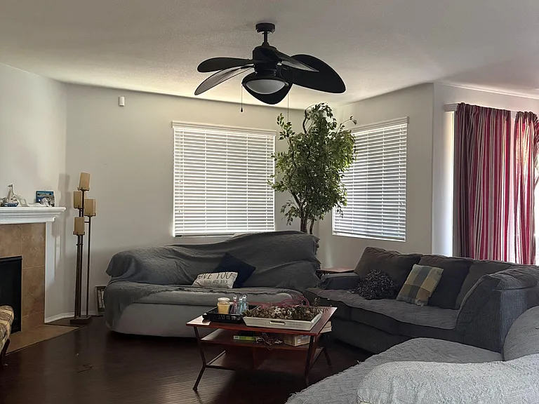 Living room with sectional seating, ceiling fan, and multiple windows with blinds for natural light and privacy.