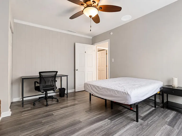Furnished bedroom with queen bed, work desk, ceiling fan, and durable wood-look flooring with easy access to the hall.