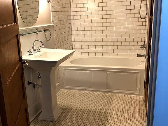 Vintage charm bathroom with hex-tile floor, beaded board wainscoting, deep bathtub with subway tile surround, and pedestal lavatory.