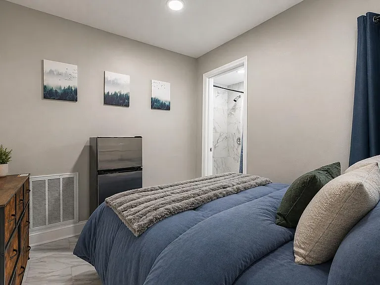 Furnished bedroom with ceiling fan, dresser storage, and convenient in-room mini fridge, plus own bathroom