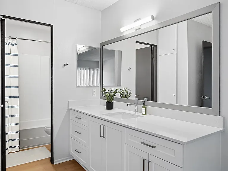 Renovated Package II bath with white quartz countertops, white cabinetry, updated hard surface flooring, and framed mirror