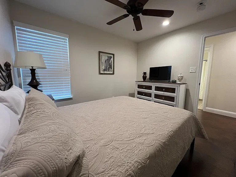 Cozy second bedroom with mounted TV, dresser storage, and abundant natural light.