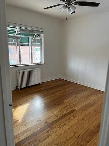 Light and bright bedroom with ceiling fan, radiator heat and lovely hardwood floors.