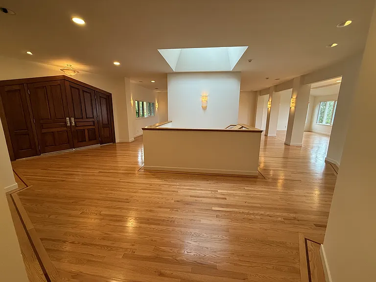 Grand living room and formal dining room featuring a fireplace, built-in buffet cabinetry, recessed lighting, rich wood flooring throughout and a wall of glass panels showcasing the bay view.