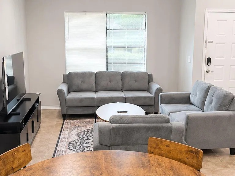 Well-sized living area with a comfortable seating setup, TV stand, and window with blinds for natural light.