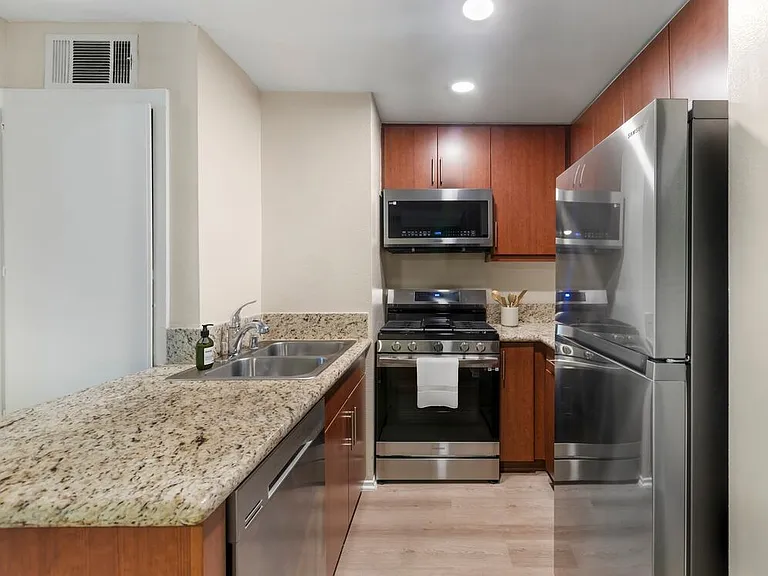 Renovated Package I kitchen with stainless steel appliances, beige speckled granite countertops, chestnut cabinetry, and hard surface flooring