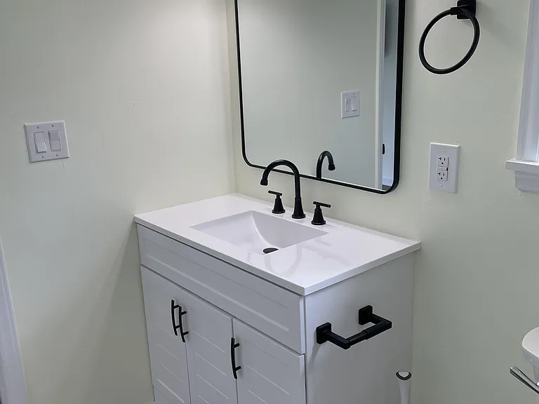 Updated bathroom vanity with integrated sink, matte-black fixtures, large framed mirror, and ample cabinet storage.