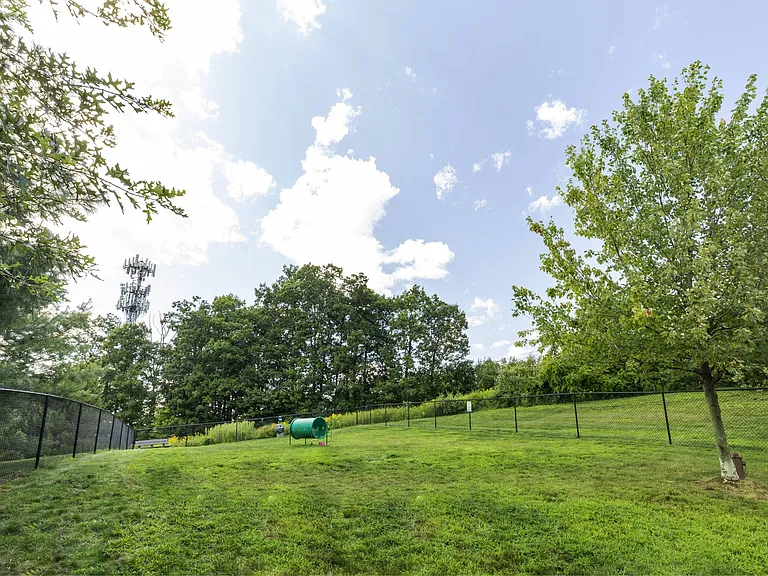 Large, fenced dog park with lush green grass, trees and obstacles for dogs at Summit Place apartments in Methuen, MA.