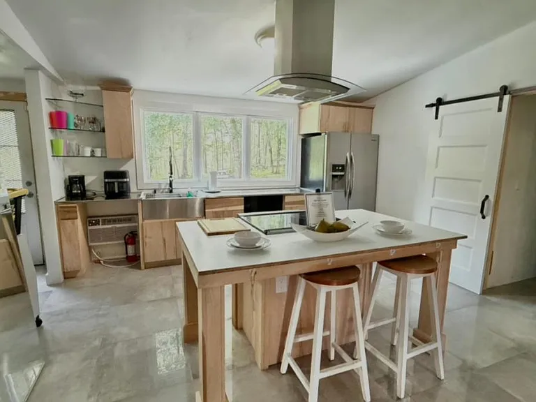 Spacious kitchen with large island seating, stainless-steel refrigerator, and a wide window over the sink.