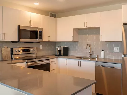Limited availability: newly renovated Finish Package II apartment homes featuring kitchens with grey quartz countertops, white cabinetry, stainless steel appliances, grey tile backsplash, and hard surface flooring - Avalon Sunset Towers