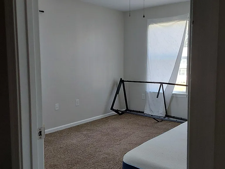 Carpeted bedroom with a ceiling fan and a window for natural light, offering a flexible layout for a bed and storage.