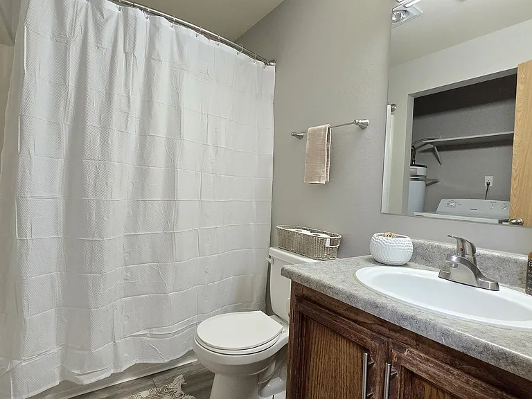 Bright, well-kept bathroom featuring a spacious vanity with ample counter space, warm wood cabinetry, and a full tub with shower. Includes convenient in-unit laundry access and a clean, functional layout.