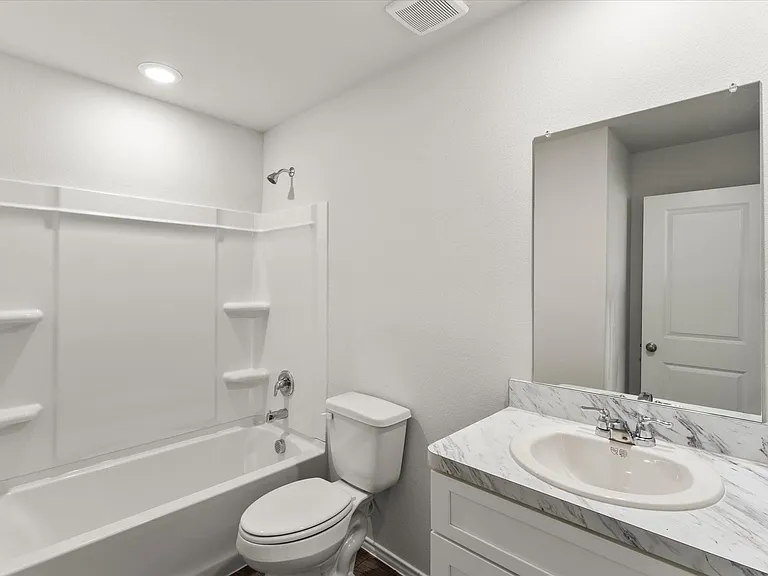 Bathroom featuring a white bathtub with a shower surround, a commode, and a vanity with a white-finish cabinet and a patterned countertop