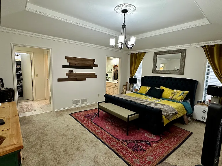 Primary bedroom with ornamental molding, an inviting chandelier, a raised ceiling, and carpet flooring