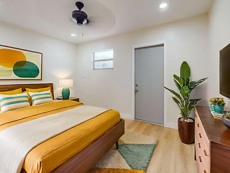 Inviting and stylish bedroom with warm tones, featuring a comfortable bed, modern artwork, vibrant plants, and sleek wooden furniture.