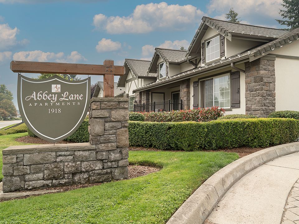 Charming entrance to Abbey Lane Apartments surrounded by manicured gardens and elegant stone features, under a picturesque sky.