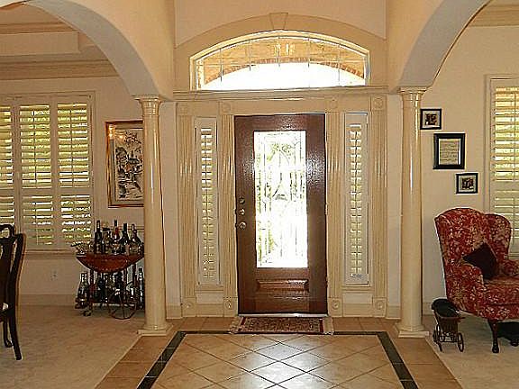  High ceiling foyer with columns on either side, wooden door with leaded glass insert and plantation shutters on the side light windows plus attractive tile flooring.