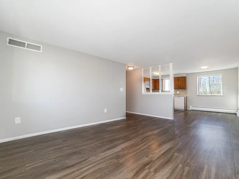Bright and spacious living area with elegant wood flooring, large windows offering natural light, and a modern, partially open kitchen with sleek cabinetry.