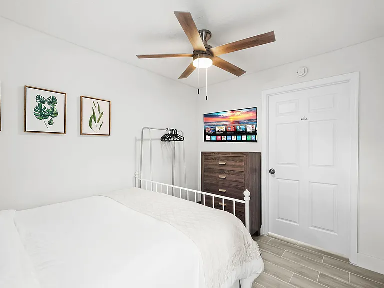 Furnished bedroom with ceiling fan, smart TV, dresser storage, and a clothing rack for easy organization.