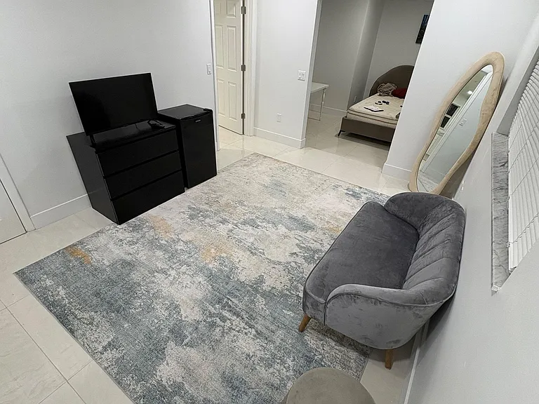 Tiled living area with seating, area rug, and space for a TV setup, plus an open connection to the bedroom area.