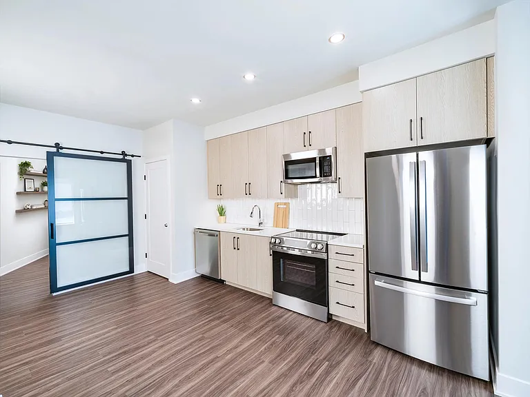 Kitchen with light wood cabinetry, quartz island seating, and stainless steel appliances arranged in a bright, open layout for daily cooking and gathering.