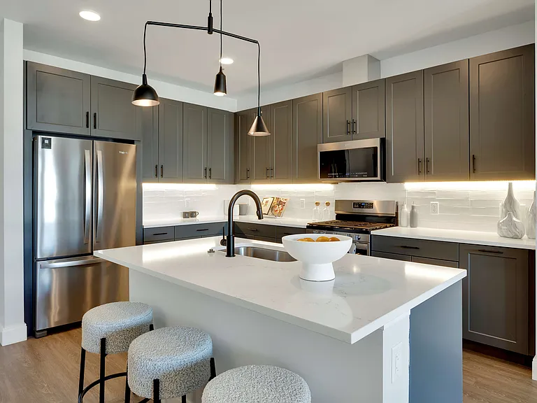 Modern kitchen with sleek dark cabinets, stainless steel appliances, and a stylish island featuring cozy stools and elegant lighting.