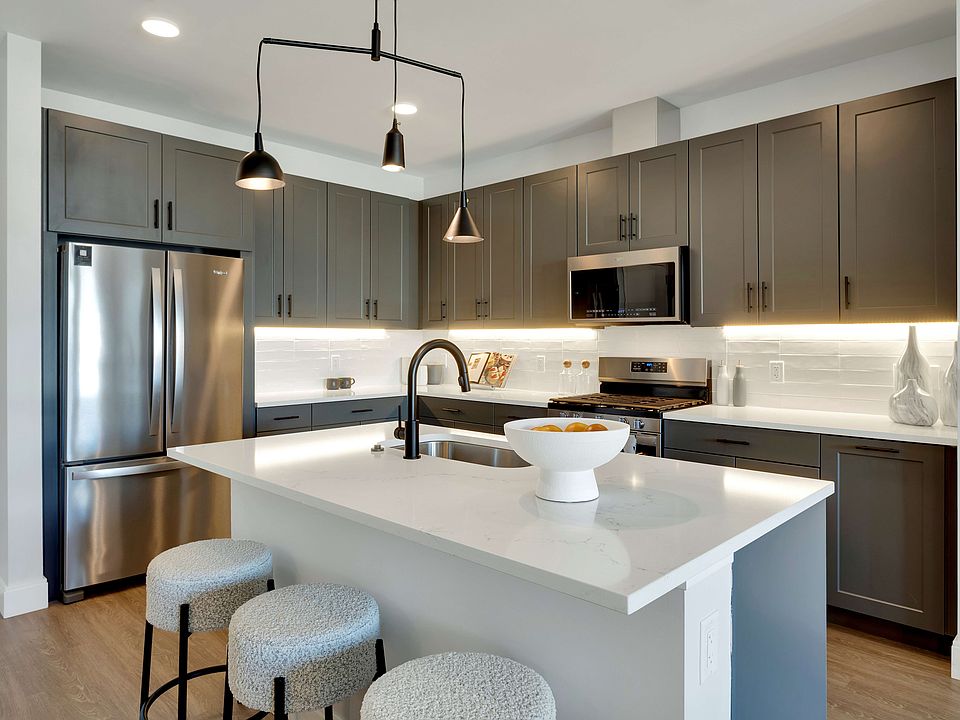 Modern kitchen with sleek dark cabinets, stainless steel appliances, and a stylish island featuring cozy stools and elegant lighting.