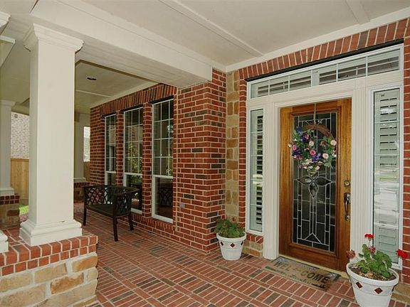 This is a better view of the quaint covered porch entry with extensive brick (allowing for easier maintenance). A leaded glass door is surrounded by windows. There is enough space for a sitting area as well.
