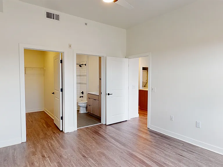 Spacious apartment bedroom with large closet, attached bathroom and wood-style flooring.